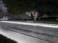 a man walks down the sidewalk in the middle of the night, while his car is parked by him