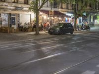 a street with many restaurants next to a small cafe on the street in front of a large building