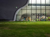 an empty building in front of a large windowed glass structure at night time with a view through the lawn