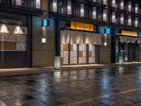 a large brick sidewalk with a store front at night time and a sign that says