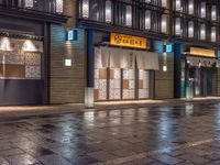 a large brick sidewalk with a store front at night time and a sign that says