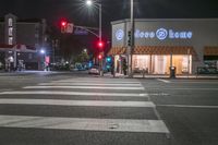 there is a crosswalk that has people walking across it at night outside a local business