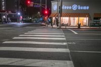 there is a crosswalk that has people walking across it at night outside a local business