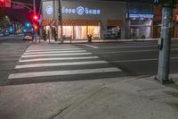 there is a crosswalk that has people walking across it at night outside a local business