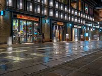 a large brick sidewalk with a store front at night time and a sign that says