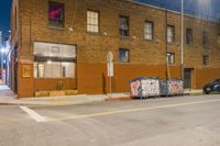 a group of parked cars near an old building at night, with a street sign and other graffiti on it