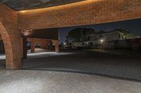 an empty walkway that has a light lit on it at night, showing an arch between two brick walls