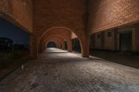 a long brick hallway is shown at night time with lights on it and brick buildings