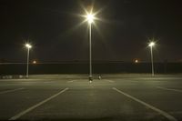 an empty parking lot lit by two street lamps at night as well as a couple walking across