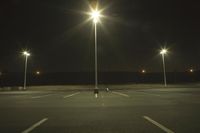 an empty parking lot lit by two street lamps at night as well as a couple walking across