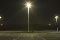 an empty parking lot lit by two street lamps at night as well as a couple walking across