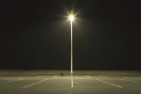 an empty parking lot lit by two street lamps at night as well as a couple walking across
