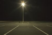 an empty parking lot lit by two street lamps at night as well as a couple walking across
