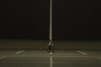 an empty parking lot lit by two street lamps at night as well as a couple walking across