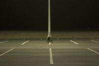 an empty parking lot lit by two street lamps at night as well as a couple walking across