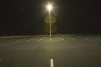 an empty parking lot lit by two street lamps at night as well as a couple walking across