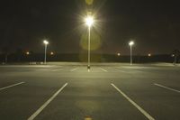 an empty parking lot lit by two street lamps at night as well as a couple walking across