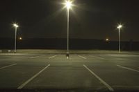 an empty parking lot lit by two street lamps at night as well as a couple walking across
