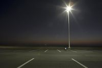an empty parking lot lit by two street lamps at night as well as a couple walking across