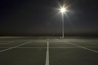 an empty parking lot lit by two street lamps at night as well as a couple walking across