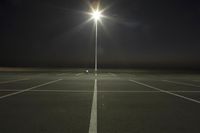 an empty parking lot lit by two street lamps at night as well as a couple walking across
