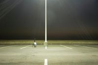 an empty parking lot lit by two street lamps at night as well as a couple walking across
