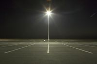 an empty parking lot lit by two street lamps at night as well as a couple walking across