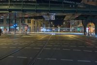 a night shot of a busy street scene with tram tracks and cars driving under a train bridge