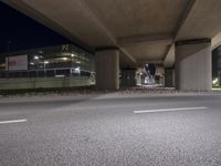 an intersection under a bridge at night with a skateboard on the ground and two traffic signs