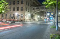 car lights streaking down an empty urban street at night with a large stone building and bridge