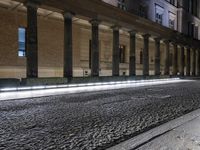 a light trail is on the side of a city street at night near buildings and pillars