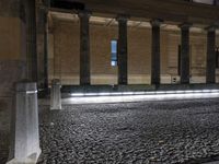 a light trail is on the side of a city street at night near buildings and pillars