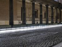 a light trail is on the side of a city street at night near buildings and pillars