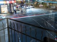 an intersection with buses, lights and shops at night time on the road side of a city street