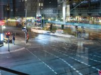 an intersection with buses, lights and shops at night time on the road side of a city street