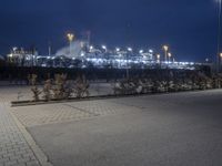 an empty street in front of a large industrial site lit up at night with many lights on it