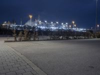 an empty street in front of a large industrial site lit up at night with many lights on it