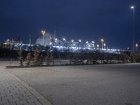 an empty street in front of a large industrial site lit up at night with many lights on it