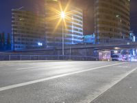 a bus is on an empty highway at night time, there are buildings in the background