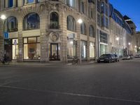 cars and bicyclists are driving along this empty street in front of many old buildings