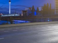 a man riding his bike along the side of a bridge over water at night with the television tower in the background