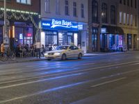 there is a car passing by a diner on a street at night, while people sit in the windows