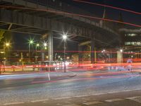 car lights travel under an elevated bridge over a city street at night as traffic passes under