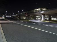 an empty city street at night with traffic lights on the street and buses parked near a bridge