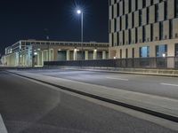 a street scene at night with an empty road under the lights, along side of a building