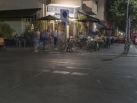 people are walking through the street outside at night time with umbrellas overhead, outside a cafe on sidewalk