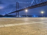 the view of a very big bridge on the water from the ground below it with lights