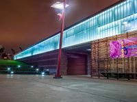 a bench and sign at the outside of a building at night with street lights all around