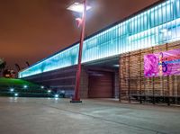 a bench and sign at the outside of a building at night with street lights all around