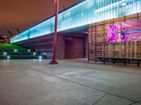 a bench and sign at the outside of a building at night with street lights all around